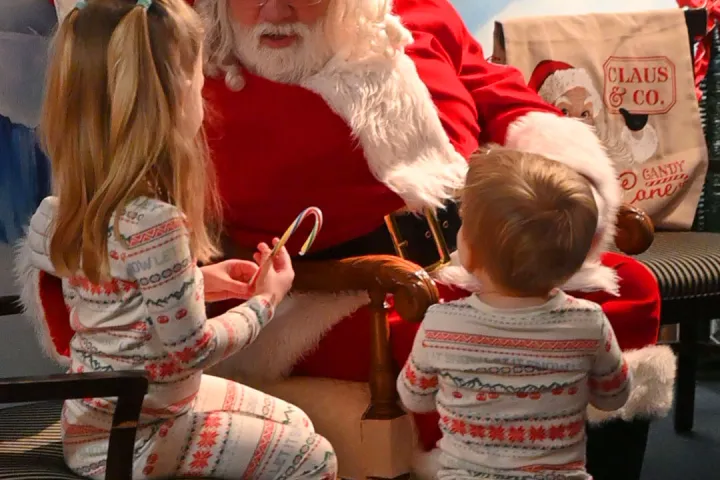 Santa Claus with two children in pajamas holding candy canes, snowy mural backdrop.