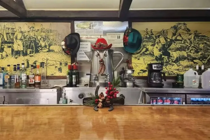 Bar counter with hats, bottles, coffee maker, and vintage wall art.