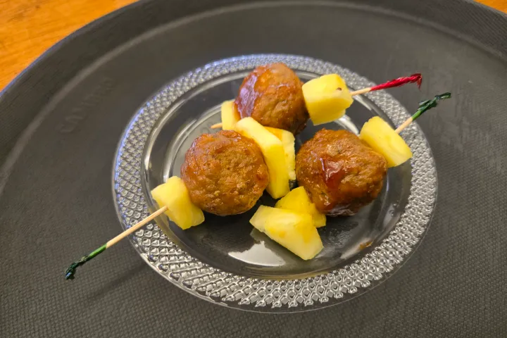 Three skewers with meatballs and pineapple chunks on a glass plate.