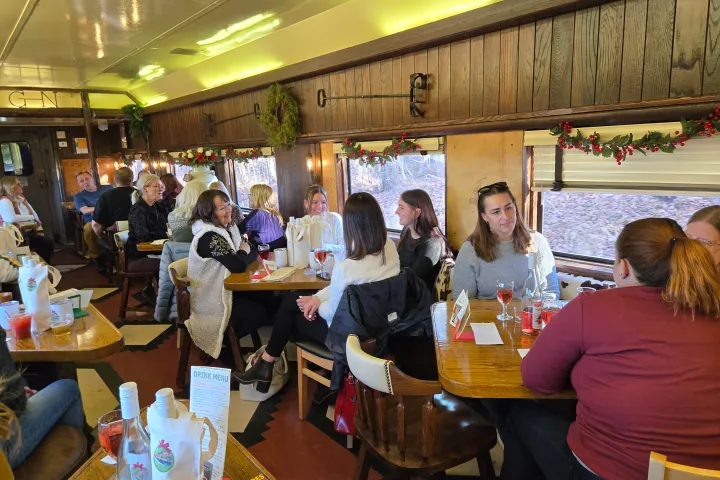 People sitting at tables inside a train car decorated with holiday garlands.