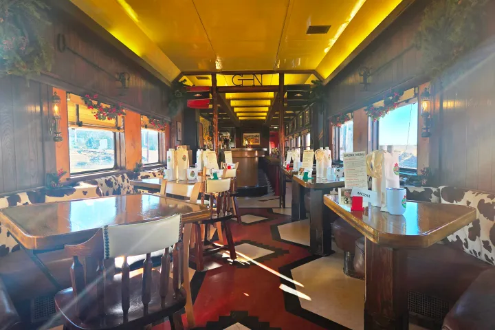 Vintage train car restaurant interior with wooden tables, cowhide seats, and holiday decorations.